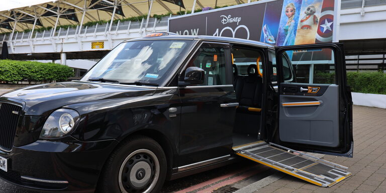 A black London taxi with its back door open and a folding ramp let down to the pavement