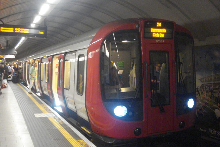 A red-fronted Tube train with its headlights on at an underground platform, the screen on its front reading Hammersmith, Circle line