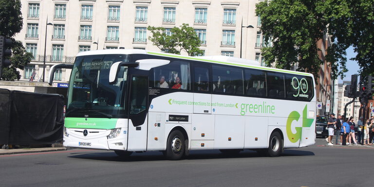 A white Green Line coach with a large green "GL" logo on its side, driving past Marble Arch in London with "Luton Airport 757" on its sign