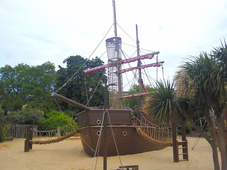 The old wooden pirate ship in the Diana Memorial Playground, with rope bridges and rigging, standing in sand among palm-like trees