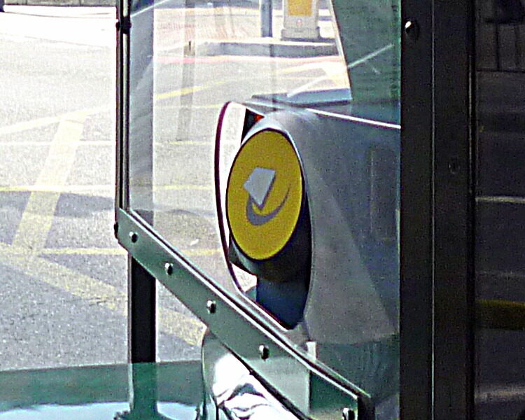 A grey card reader with a yellow Oyster target beside a London bus driver's cab, seen through the cab's glass