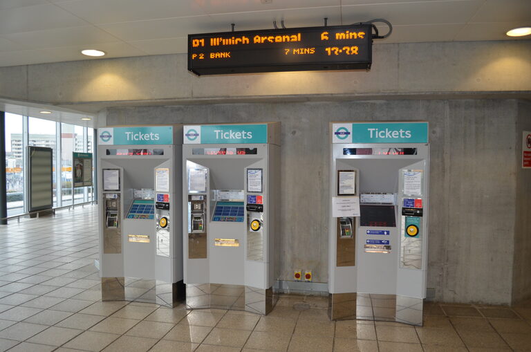 Three DLR ticket machines under a departures board in London City Airport's DLR station