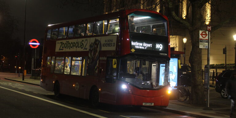 A red double-decker bus with "Heathrow Airport Terminal 5 N9" lit up on its front sign, at a bus stop on a dark street at night