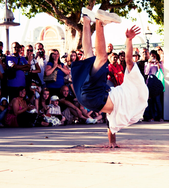 A breakdancer balancing on one hand in front of a crowd on the riverside walk