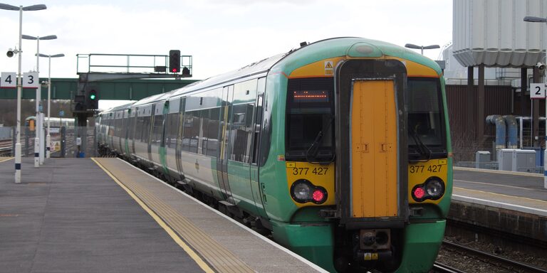 The yellow back end of a green and white Southern train pulling away from an empty platform at Gatwick Airport station