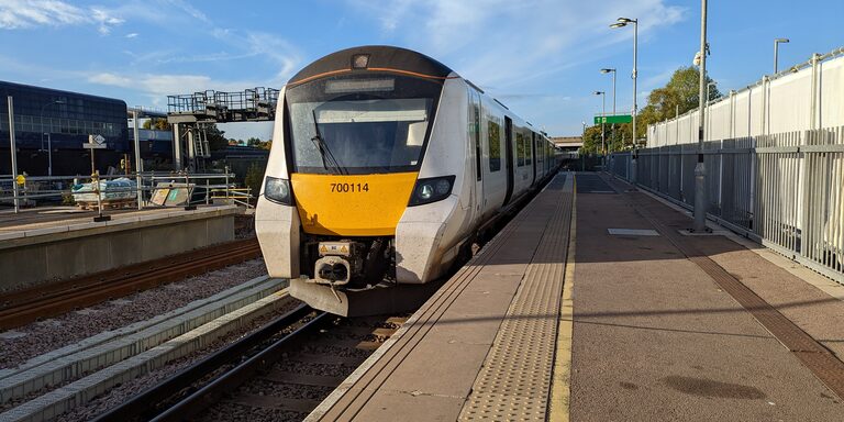 A white Thameslink train with a yellow front waiting at an empty platform at Gatwick Airport station on a sunny day