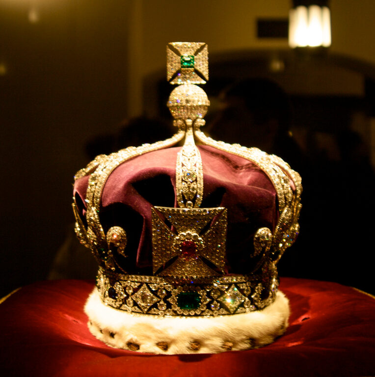 A gold crown set with jewels, with a red velvet cap and white ermine band, on a red cushion