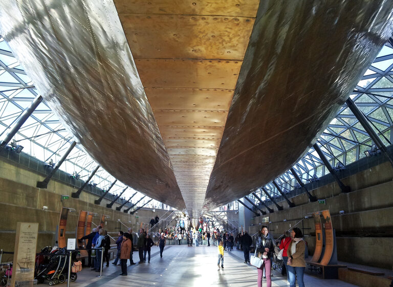 Visitors walking along under the ship's golden hull, with the glass canopy sloping down on both sides