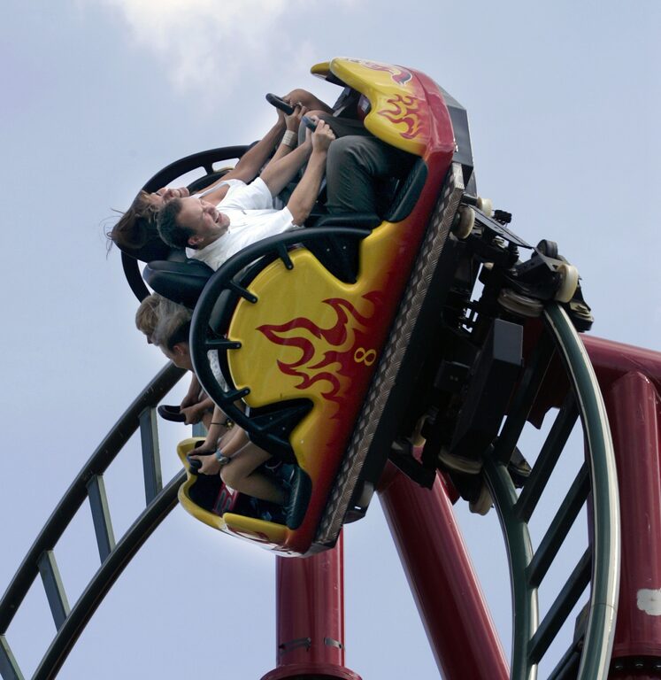 A yellow rollercoaster car painted with red flames, tilted on its track with riders inside