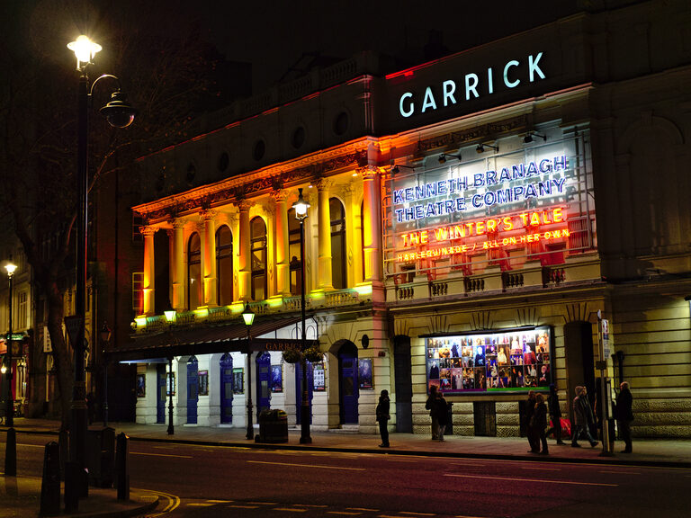 The Garrick Theatre at night, its front lit gold, with a neon sign for the Kenneth Branagh Theatre Company's The Winter's Tale