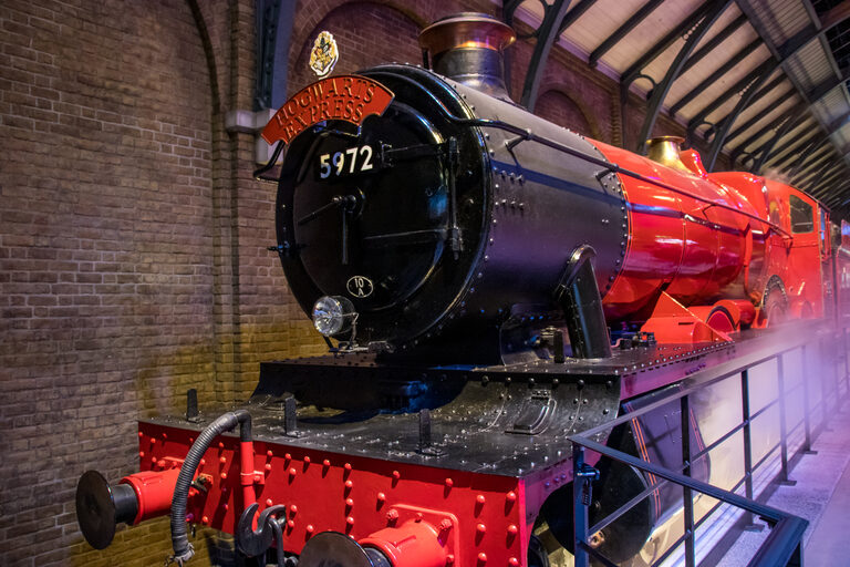 The red and black Hogwarts Express steam engine, number 5972, beside a brick wall under an arched station roof