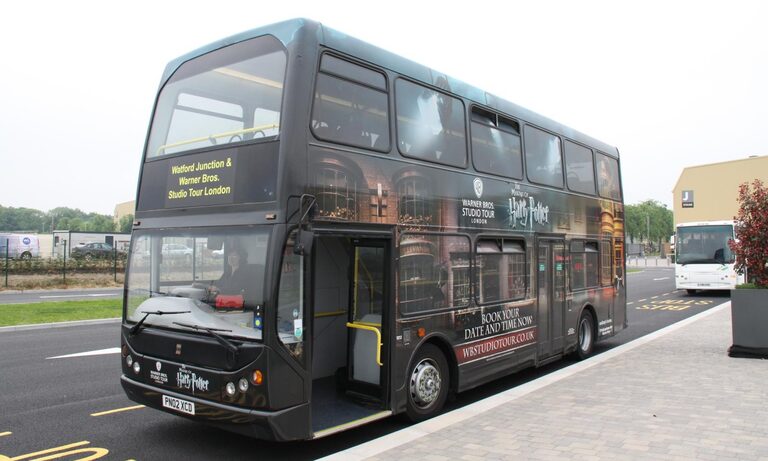 A black double-decker bus painted with Harry Potter scenes, its sign reading "Watford Junction & Warner Bros. Studio Tour London", at a bus stop