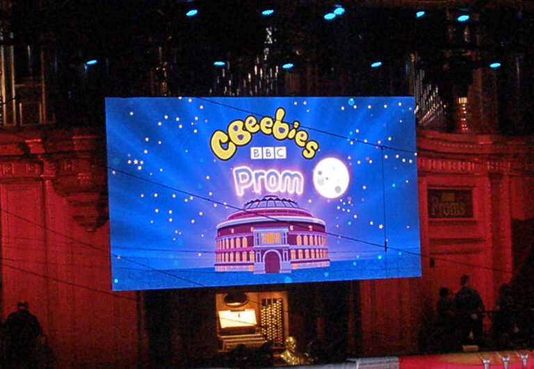 The big screen above the stage showing the CBeebies Prom title, a cartoon Royal Albert Hall and the moon, with the organ behind