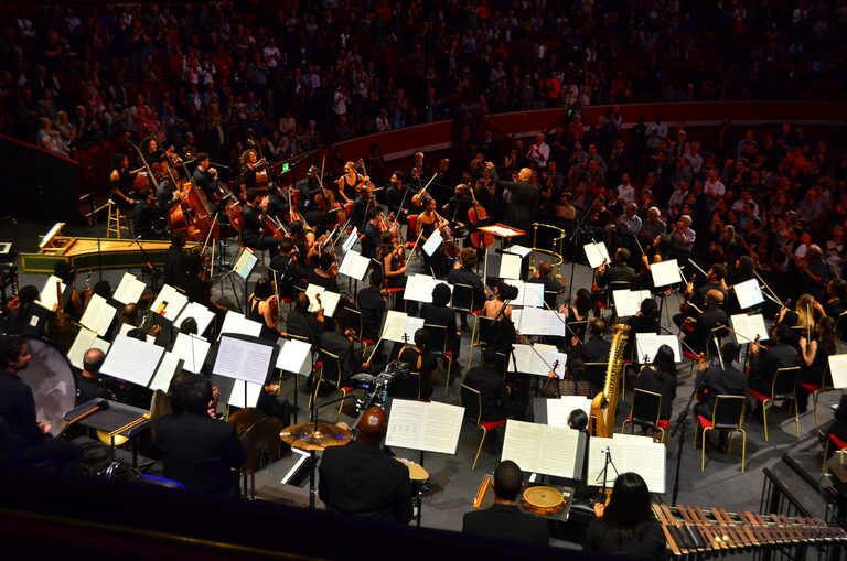 An orchestra on the stage seen from high up in the hall, with the audience in the seats behind it
