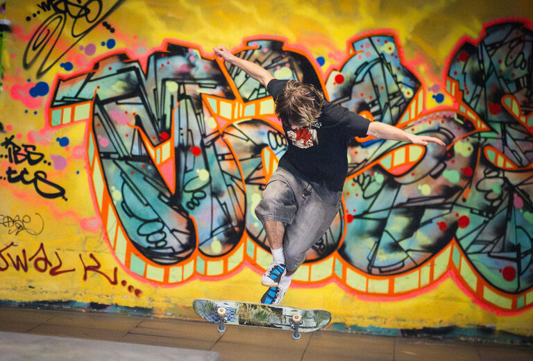 A skateboarder mid-jump in front of graffiti in the Undercroft
