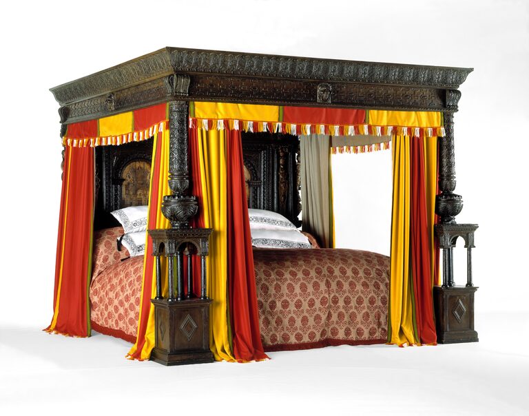 A huge carved oak four-poster bed with red and yellow striped curtains